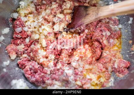 Macrofano piano primo piano di manzo crudo rosso macinato in acciaio inox recipiente di miscelazione con cipolle uovo e spezie per la cottura di polpette ricetta mescolato con w Foto Stock