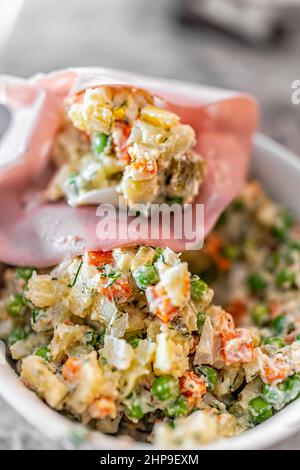 Tradizionale insalata russa di patate chiamata olivie olivier macro closeup wrapes in mortadella deli fetta con lessato patate a dadini, carote, piselli e su Foto Stock