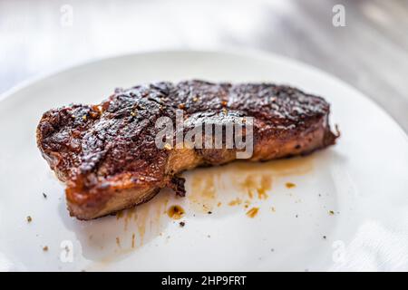 Striscia di New York cotta alla griglia di media rara, alimentata all'erba, o bistecca di manzo ribeye su piatto bianco Foto Stock