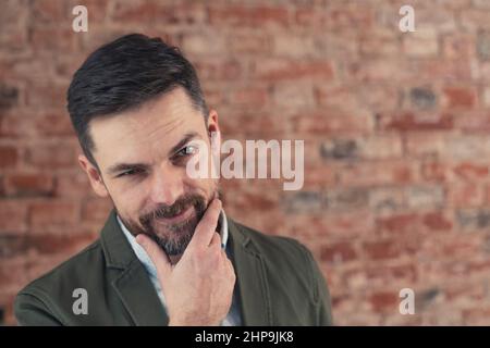 Uomo europeo a metà 30s che indossa un vestito flirtatiously sollevando il suo sopracciglio sopra il fondo della parete del mattone. Foto di alta qualità Foto Stock