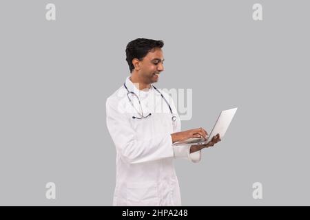 Medico che usa laptop isolato. Medico indiano maschio con portatile in mani. Foto Stock