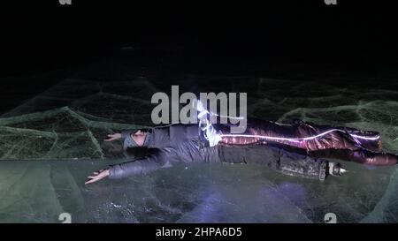 Giovane coppia amorevole pattinare alla pista di pattinaggio di notte. Uomo e donna baciano, abbracciano, si divertono, imparano a pattinare. Fare l'amore su ghiaccio. Bel ghiaccio limpido con crac Foto Stock