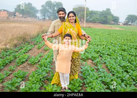 Ritratto Happy rurale indiano famiglia in piedi in campo agricolo, sorridente giovane agricoltore maschio in piedi con suo figlio e moglie. Foto Stock