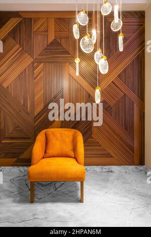 Moderna poltrona arancione e contemporaneo lampadario in vetro, in una sala con pareti decorate in legno e pavimento in marmo bianco Foto Stock