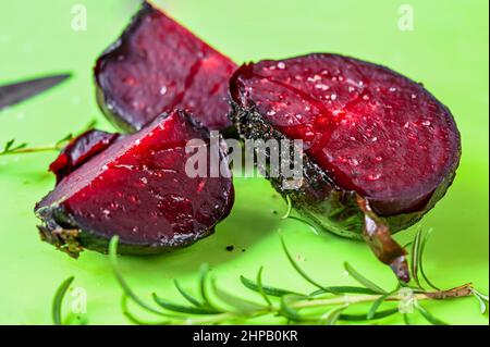 Barbabietola da forno a fette su tavola da cucina verde, ramoscello di rosmarino. Foto Stock