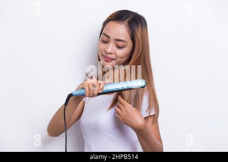 giovane asiatico bella donna felice capelli raddrizzando con capelli piastra su sfondo bianco Foto Stock