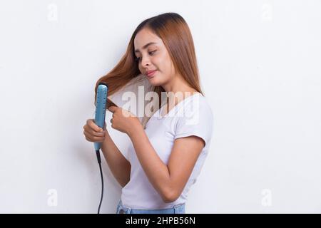 giovane asiatico bella donna felice capelli raddrizzando con capelli piastra su sfondo bianco Foto Stock