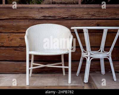 Mobili in rattan bianchi vuoti, sedie da giardino all'aperto e tavolo laterale rotondo sullo sfondo della parete in legno di legno naturale della terrazza. Foto Stock