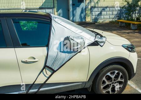 Un'auto in un parcheggio con un parabrezza coperto con un riflettore parasole all'esterno, per proteggere la parte in plastica dell'abitacolo e il Gl Foto Stock