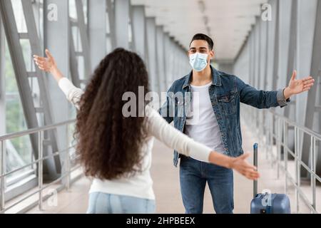 Happy Arab Guy indossare maschera medica incontro ragazza in aeroporto dopo l'arrivo Foto Stock