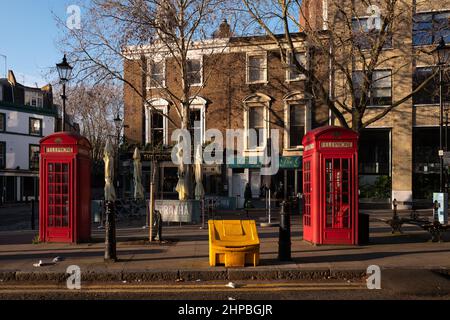 Il sole della mattina presto cade su un bidone di sale giallo e due tradizionali cabine telefoniche rosse di Londra Foto Stock