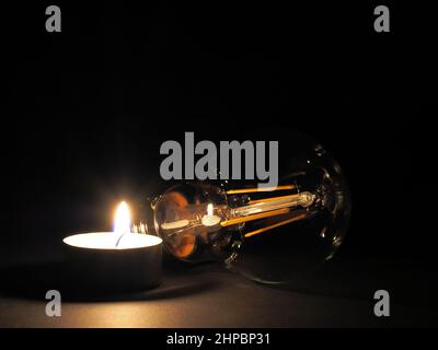 Candela che brucia accanto ad una lampadina. Concetto di aumento dei costi energetici, povertà e carenza di energia Foto Stock