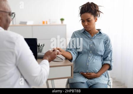 Medico nero esperto maturo che dà le pillole alla signora incinta triste Foto Stock