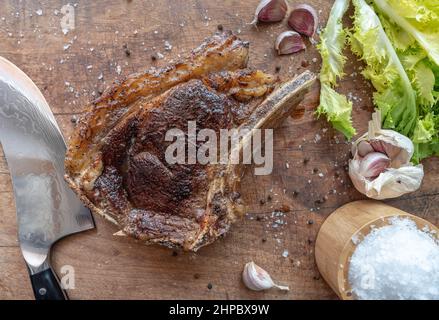 Sous Vide cotto medio-raro bistecca di manzo rubia gallega stagionata secca con coltello, scaglie di sale marino, aglio, pepe e insalata su un asse di legno Foto Stock