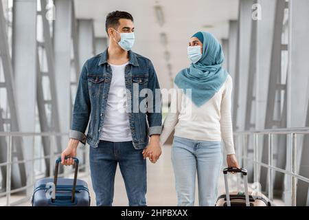 Coppia musulmana felice che indossa maschere mediche protettive Passeggiate con i bagagli in aeroporto Foto Stock