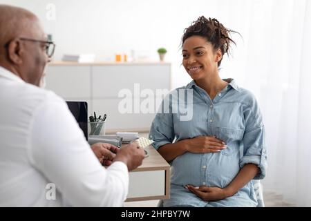 Maturo esperto medico nero che mostra pillole a donna incinta Foto Stock