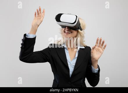 Aziende e tecnologie. Giovane donna d'affari in visore VR che sperimenta la realtà virtuale su sfondo grigio chiaro Foto Stock