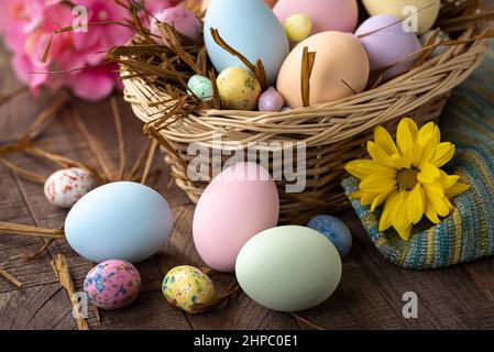 Uova di Pasqua color pastello e caramelle in un cestino e su un rustico tavolo in legno con fiori colorati Foto Stock