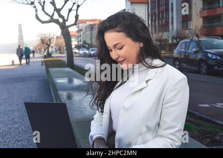 Giovane donna caucasica che lavora con un computer portatile su una passeggiata sulla spiaggia. Foto Stock