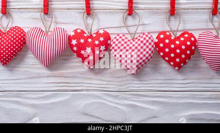 Cuori di tessuto valentini appesi su corda su sfondo bianco di legno Foto Stock