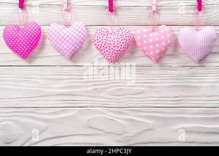 Cuori di tessuto valentini appesi su corda su sfondo bianco di legno Foto Stock