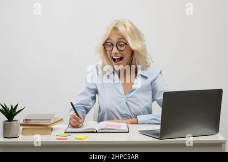 Sorpresa donna d'affari che lavora sul laptop e prende appunti in notebook, sorprendentemente leggendo le sue notazioni sul posto di lavoro Foto Stock