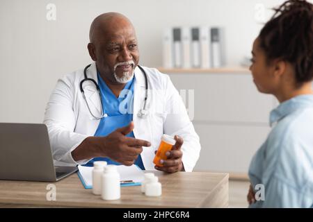 Medico nero esperto che mostra pillole a paziente femminile Foto Stock