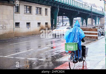 Berlino, Germania. 20th Feb 2022. Sotto la pioggia, una persona che indossa un impermeabile corre in bicicletta lungo Schönhauser Allee. Credit: Annette Riedl/dpa/ZB/dpa/Alamy Live News Foto Stock