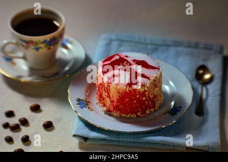 Concetto di colazione con torta Louise su un piatto di ceramica, caffè in una tazza di fedi sullo sfondo, caffè sparso in chicchi di caffè su un tavolo Foto Stock