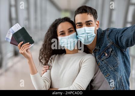 Viaggi pandemici. Coniugi mediorientali che indossano maschere protettive che portano Selfie all'aeroporto Foto Stock