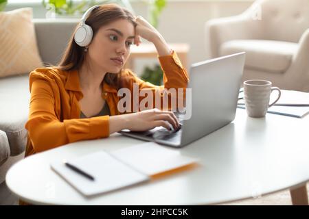 Giovane donna seria con un notebook che indossa le cuffie, lavora o studia online, con una chat video in ufficio Foto Stock