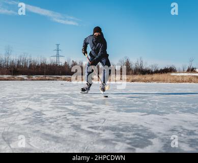 Ragazzo adolescente che gioca hockey su ghiaccio sul laghetto ghiacciato il giorno d'inverno in Canada. Foto Stock