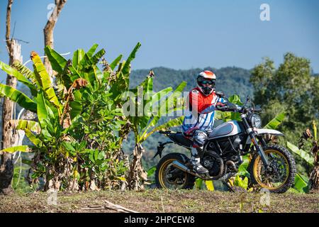 Uomo con il suo tipo di moto scrambler su terreno accidentato in Thailandia Foto Stock