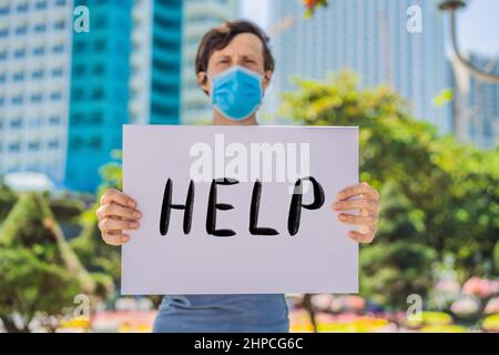 L'uomo in maschera medica previene la malattia di coronavirus tiene un poster AIUTO testo scritto a mano - lettering isolato su bianco. Concetto di Coronovirus COVID 19 Foto Stock