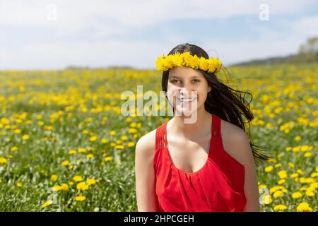 Ridendo giovane ragazza in posa in un prato di dente di leone con una corona di dandelioni sulla sua testa. Foto Stock