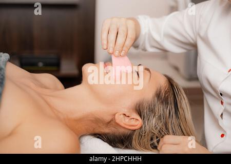 Giovane donna durante il tradizionale massaggio viso antirughe tonificante Gua Sha. Primo piano. Trattamenti di bellezza SPA. Anti invecchiamento Foto Stock