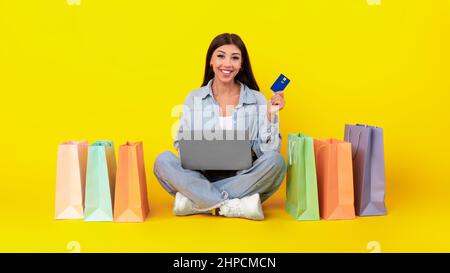Concetto di pagamento online. Sorridente giovane donna con carta di credito di debito e con l'uso di un computer portatile, ordinando abiti e acquisti via internet, seduto sul fl Foto Stock