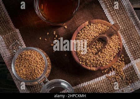 Ciotola di semi di fieno e tè giallo fieno egiziano o bevanda Methi Dana su sfondo di legno scuro Foto Stock