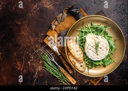 Insalata con camembert alla griglia, rucola, toast e rosmarino in un piatto. Sfondo scuro. Vista dall'alto. Spazio di copia Foto Stock