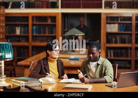 Ritratto della vista frontale di due studenti adulti in biblioteca del college che studiano insieme e usano il computer portatile Foto Stock