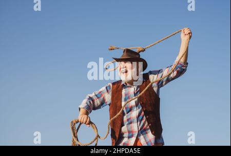 Cowboy occidentale senior che lancia la corda di lazo. Uomo selvatico bearded occidentale con giacca marrone e cappello che cattura cavallo o mucca. Rodeo o ranch. Foto Stock