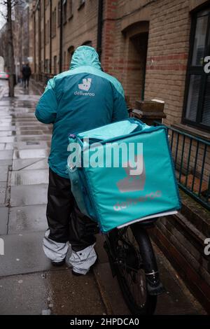 Deliveroo conducente adiacente alla sua moto in una giornata di inverni bagnati a Londra. Tramite un'app, chiunque può ordinare il take away per essere consegnato a casa propria. Foto Stock