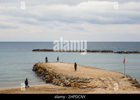 Vista ad alto angolo della spiaggia in inverno con persone in piedi su un frangiflutti rocciosi, Sanremo, Imperia, Liguria, Italia Foto Stock