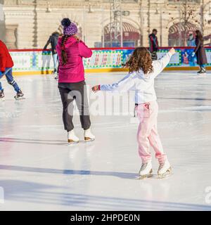 Felice ragazza pattinaggio su ghiaccio sulla pista di pattinaggio nel parco della città. Sano inverno attività all'aperto Foto Stock