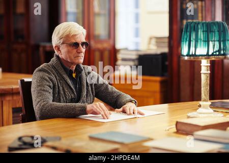 Ritratto dell'uomo anziano con libro di lettura di disturbi della vista in braille al tavolo della biblioteca classica Foto Stock