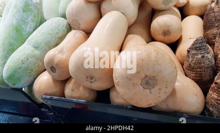 Le zucche di butternut sono poste su scaffali per la vendita insieme ad altri prodotti agricoli. Foto Stock