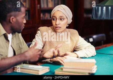 Ritratto di giovane donna con foulard mentre studia con un amico in biblioteca classica Foto Stock