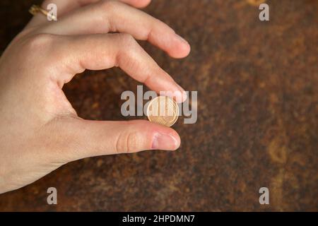 Mano femmina che tiene una moneta su uno sfondo di vecchio metallo, mano femmina con una moneta Foto Stock