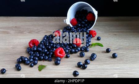 Profumo di mirtilli dolci e succosi, lamponi sparsi da un secchio su sfondo di legno. Il concetto di mangiare sano in estate. Foto Stock