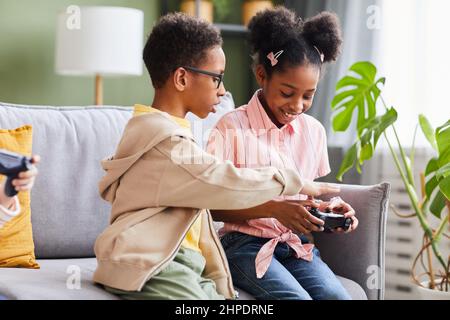 Ritratto di fratello afro-americano e sorella giocare video giochi a casa insieme Foto Stock